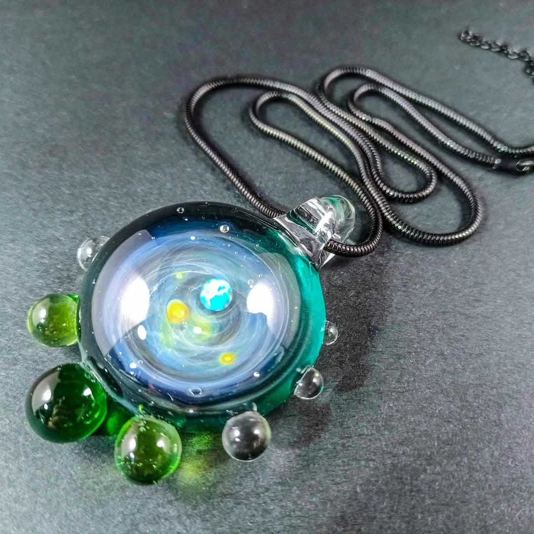 Handmade galaxy glass pendant necklace with a floating opal planet and green glass accents on a black chain — space jewellery made in Greece